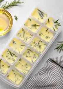 Ice cube tray with herbs frozen in oil and fresh rosemary
